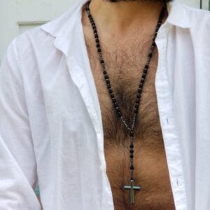 Man wearing a black onyx rosary style necklace with a hematite cross pendant over an open white shirt
