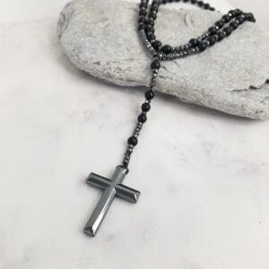 Black onyx rosary style necklace laid beside a pale stone, hematite cross resting on marble